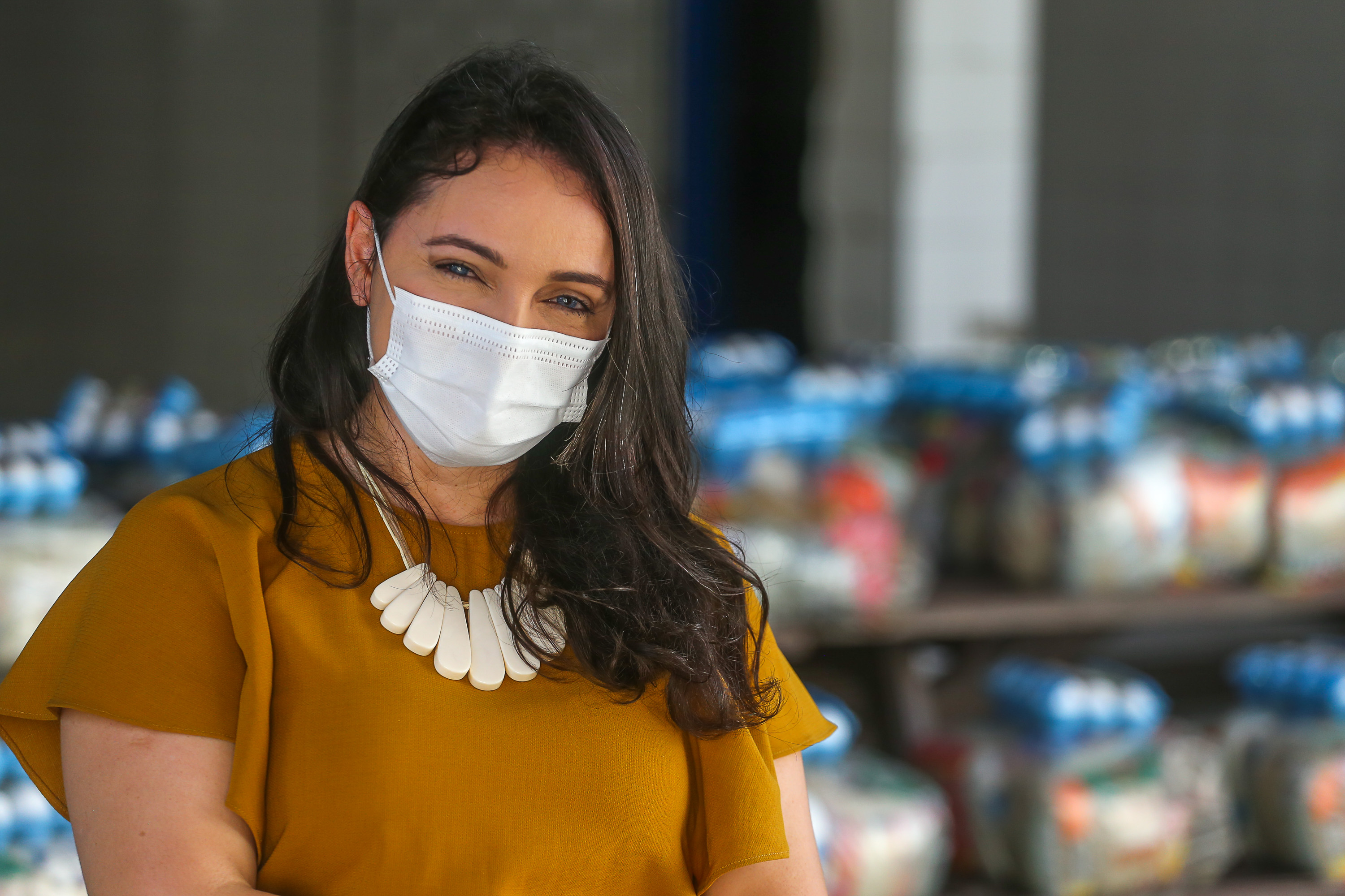 mulher de máscara posando para a foto com kits alimentares ao fundo